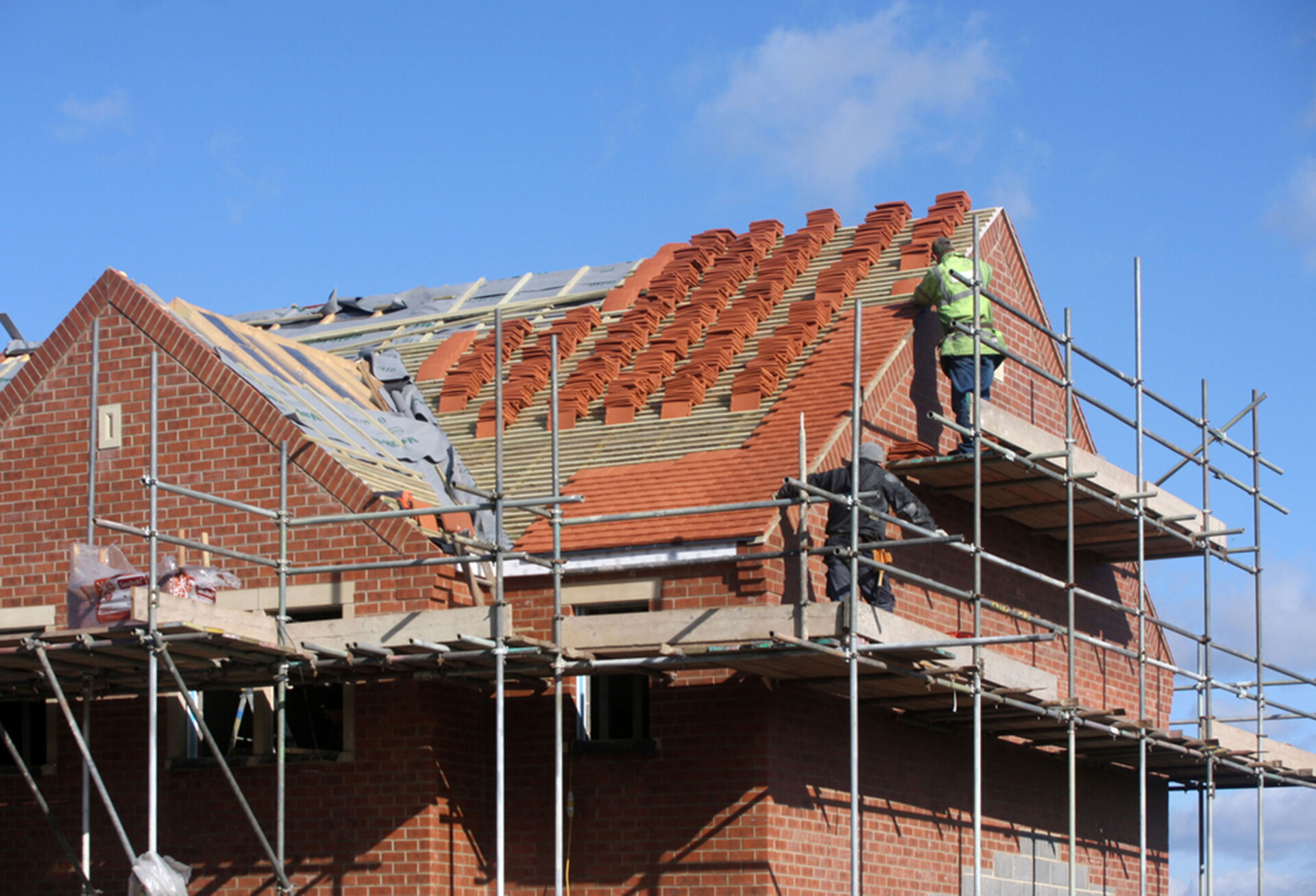 man werkt aan dak van nieuwbouwwoning in de stijgers